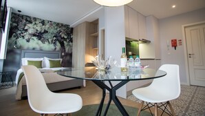 Une chambre moderne avec une table à manger en verre, des chaises blanches, un lit avec des coussins verts et une fresque murale.