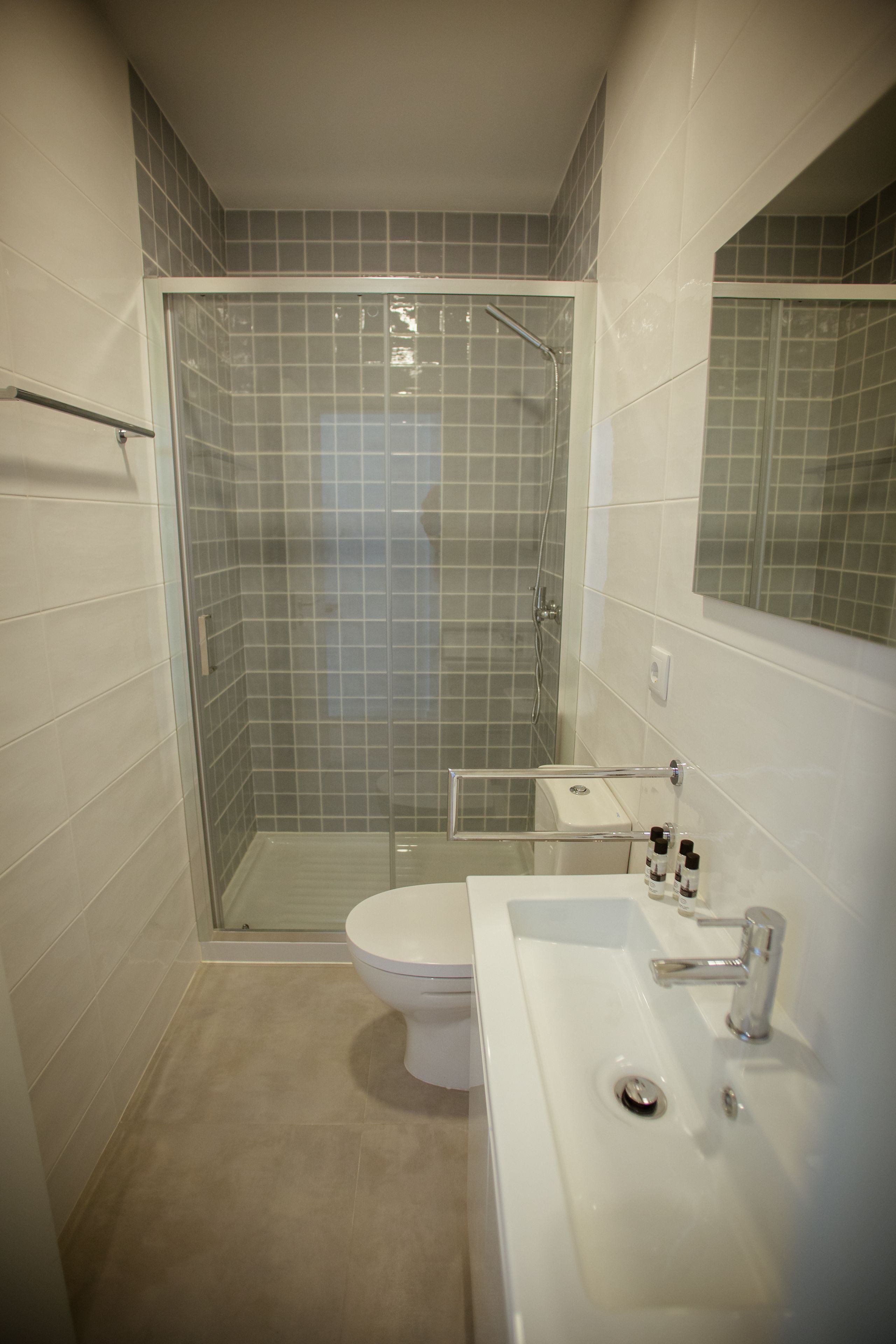Un baño moderno con ducha de vidrio, inodoro blanco y lavamanos con espejo.