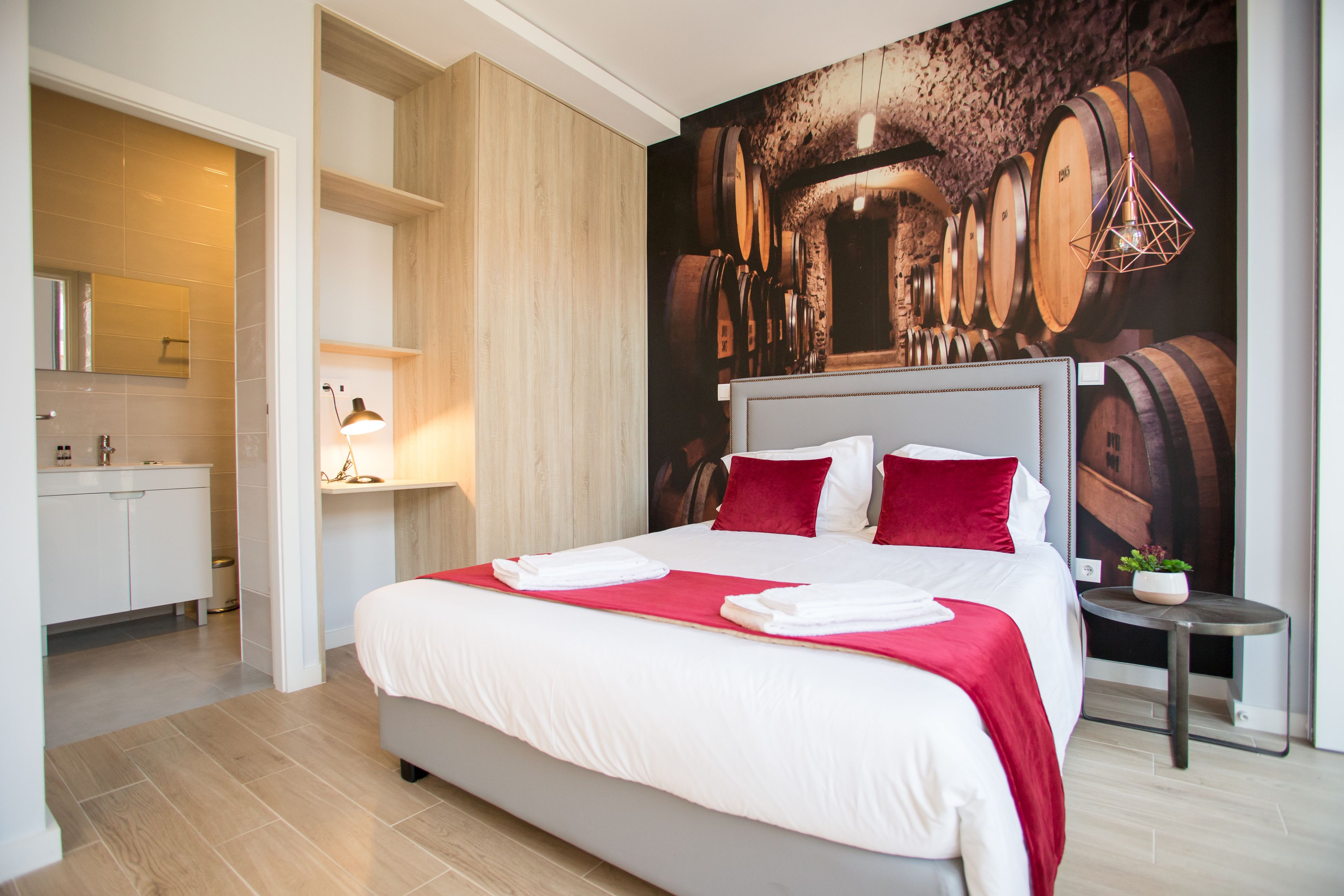 Ein modernes Hotelzimmer mit einem großen Bett, einem Holzkopfende, einer roten Akzentwand und einer Wandmalerei mit Weinfässern.