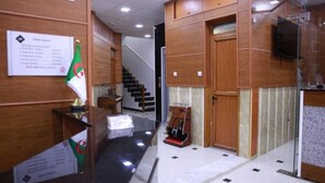A hotel reception area with a wooden reception desk, a flag, and a staircase leading to another floor. - Hotel Palace Biskra (Biskra)