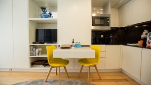 A modern kitchen with white cabinets, a microwave, and a coffee machine. There are two yellow chairs and a white table. - Almada Story Apartments by Porto City Hosts (Porto)