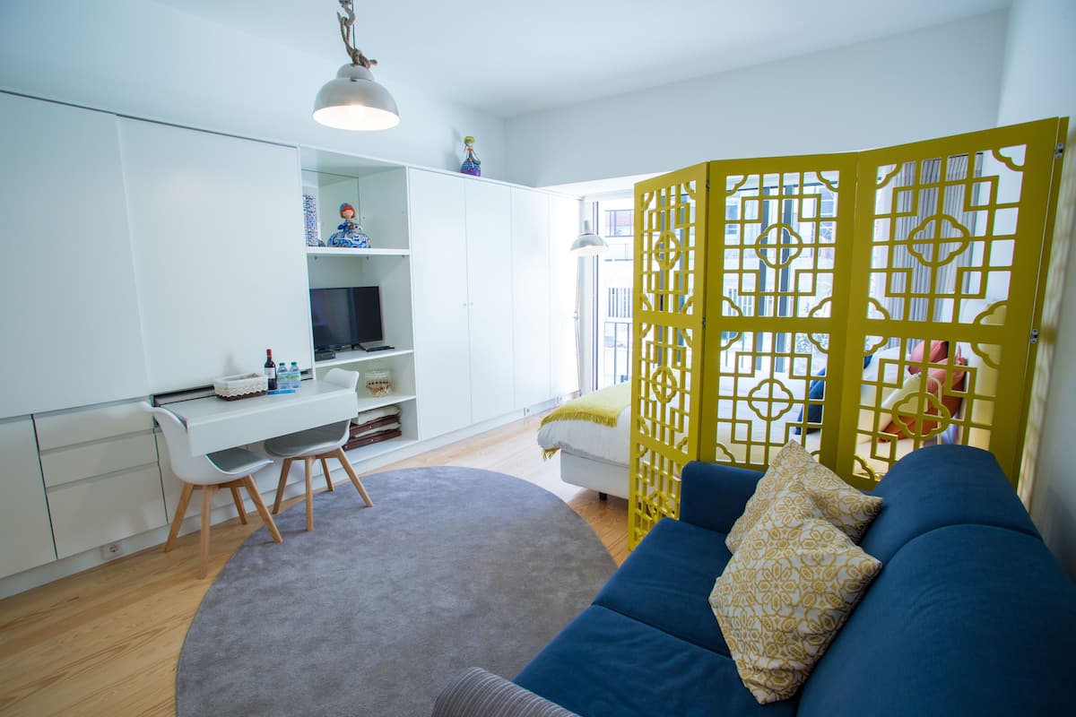 Un salon moderne avec un canapé bleu, un bureau blanc et une cloison jaune.