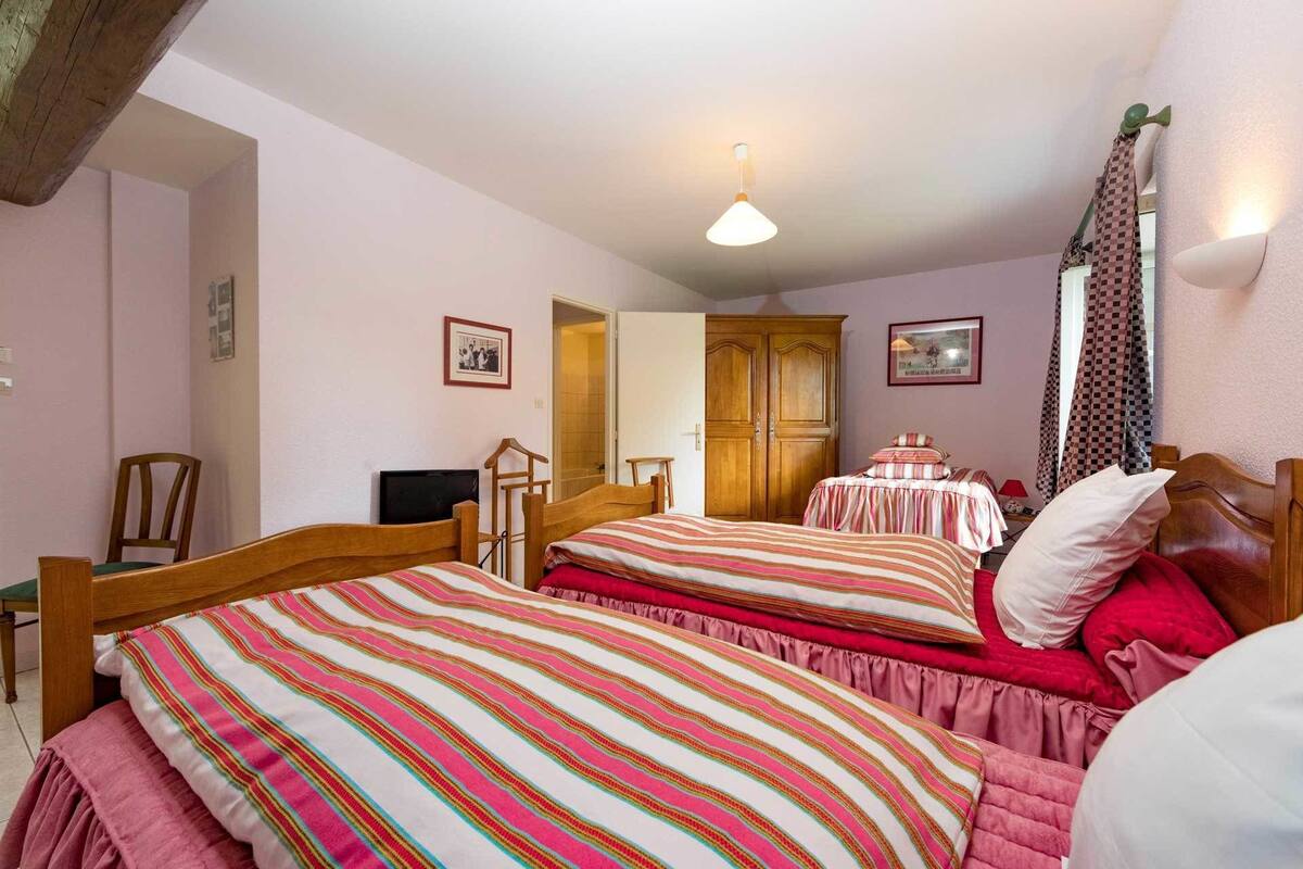 Ein Schlafzimmer mit zwei Betten, einem Holzschrank, einem Sessel und einer Deckenleuchte.