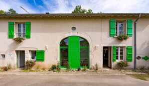 A building with a large arched entrance, green shutters, and flower boxes. - Bienvenue au Pays de Jeanne (Soulosse-sous-Saint-Élophe)