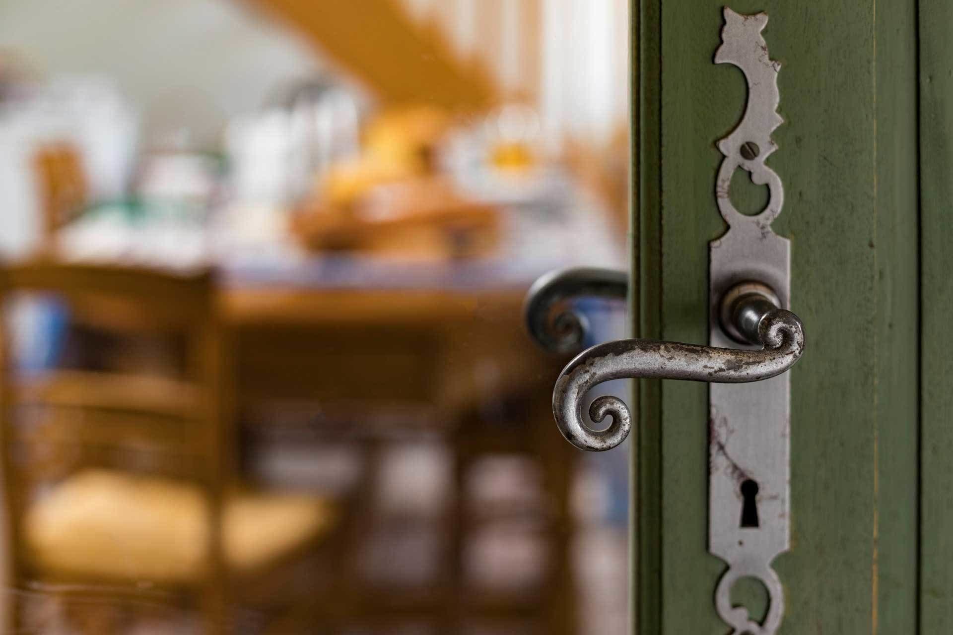 Detalhe de uma maçaneta com fechadura, emoldurada por uma porta verde.