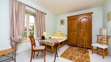 Un dormitorio con cama, un armario de madera, una mesa con lámpara, una silla y una ventana con cortinas.