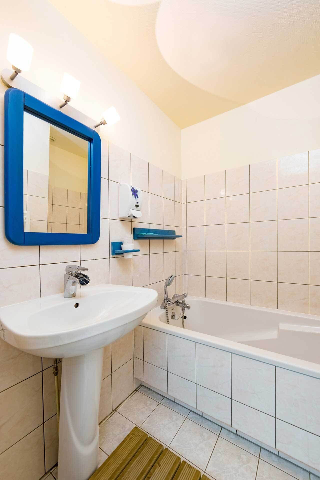 Une salle de bain avec un lavabo blanc, un miroir, une baignoire et des étagères bleues.