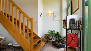 A staircase with wooden railings, a wall-mounted shelf with books and decorative items, and a variety of potted plants.