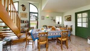 A dining area with a table set for four, surrounded by wooden chairs. A staircase is visible to the left, and a green door is on the right.