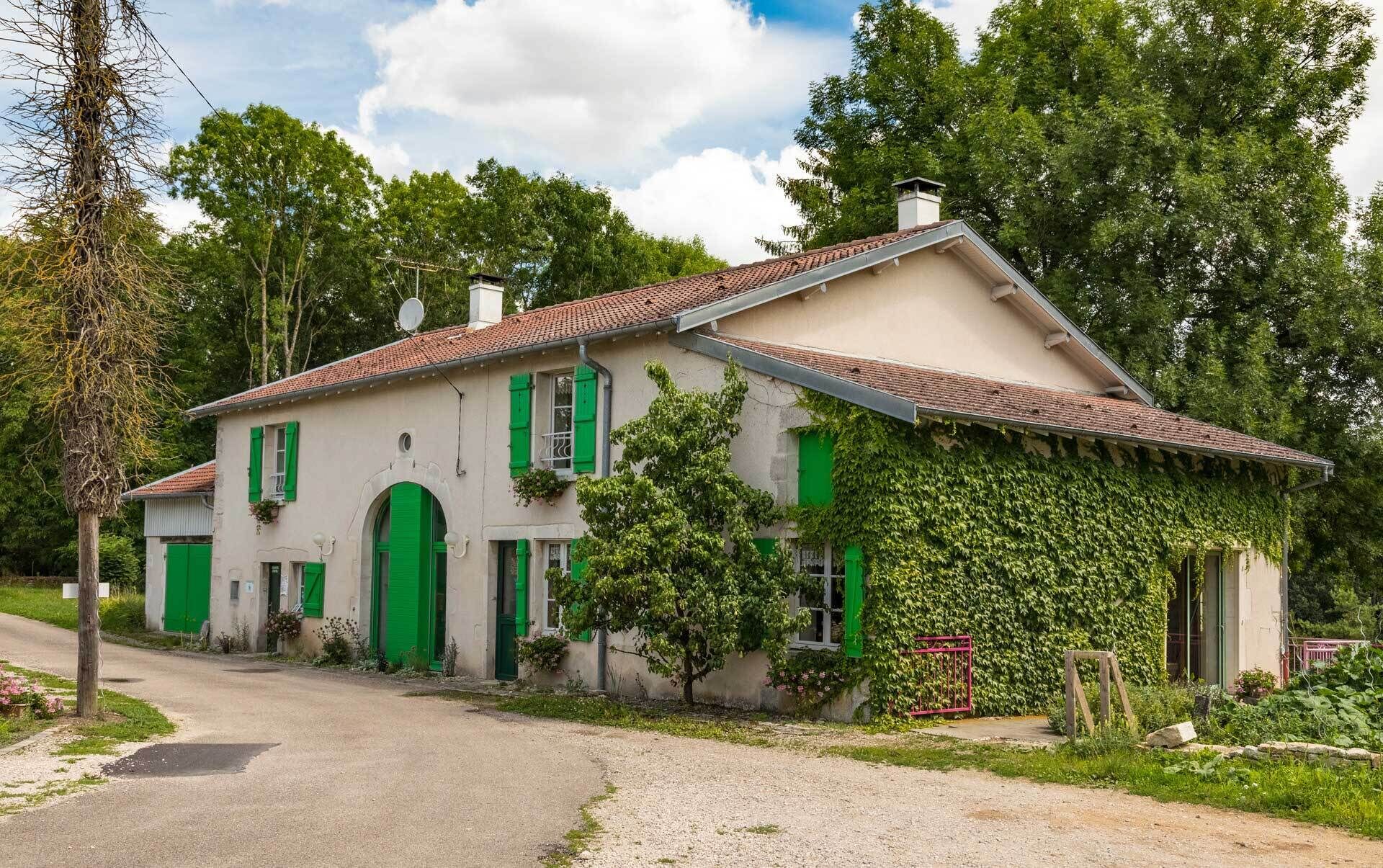 A two-story house with a tiled roof, green shutters, and a garden.