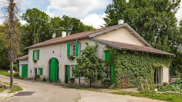 A two-story house with a tiled roof, green shutters, and a garden.