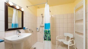 A bathroom with a sink, mirror, shower, and a chair.
