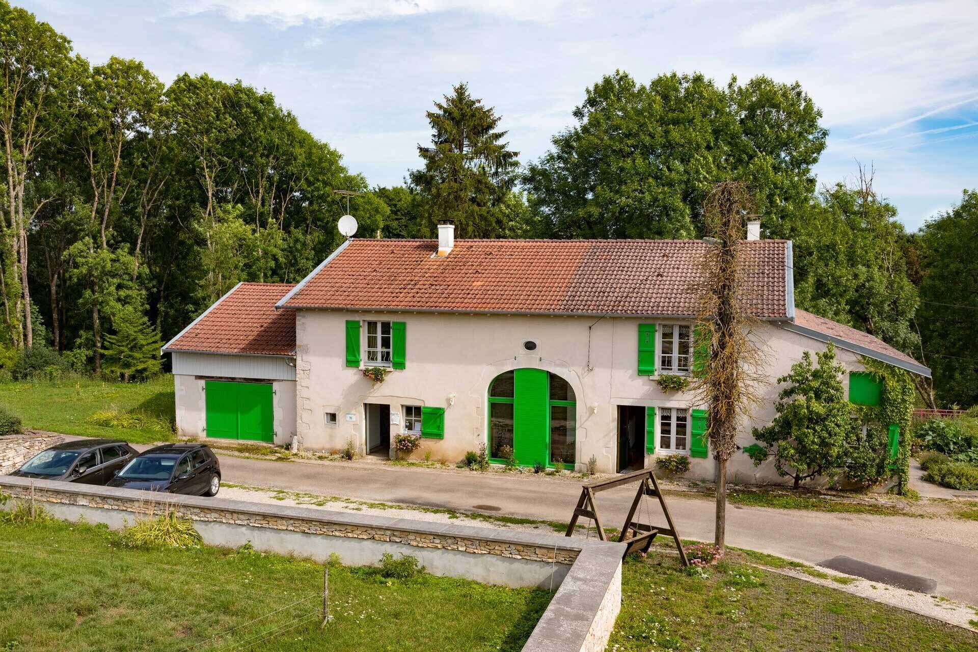 A two-story house with a red-tiled roof, green shutters, and a stone foundation.