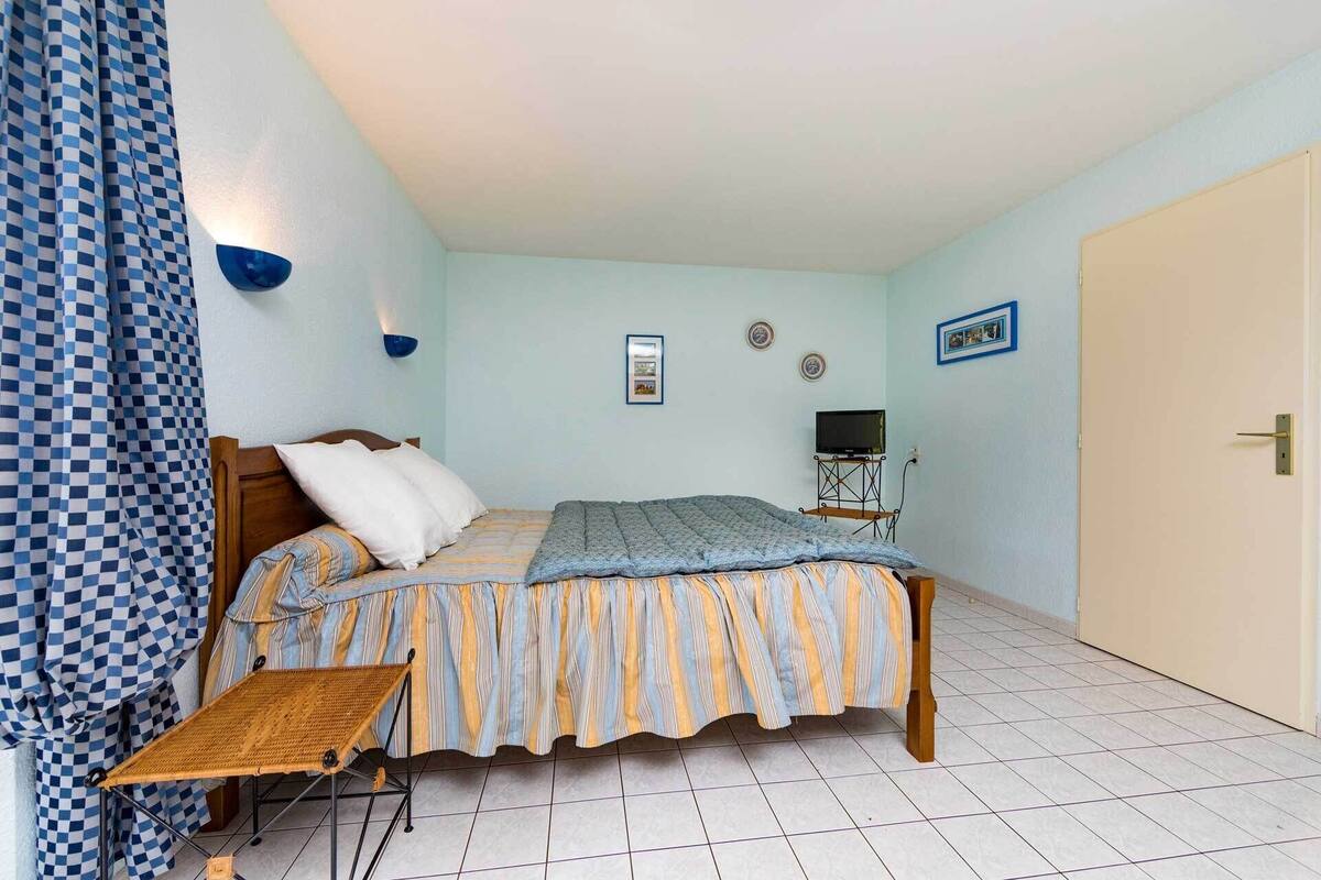 Ein Schlafzimmer mit einem Bett, einem Fernseher auf einem Schrank, einem kleinen Tisch und einer Tür.