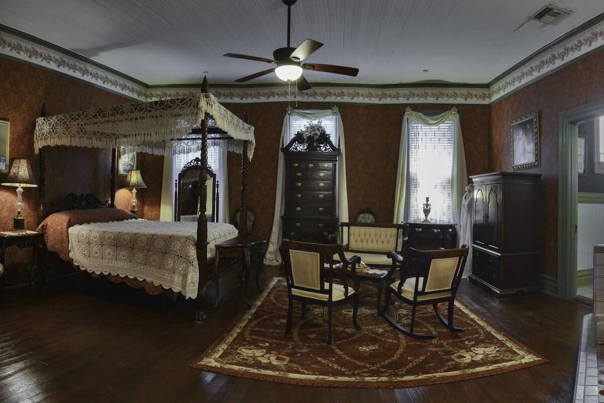 Une chambre traditionnelle comprenant un lit, un coin salon avec des fauteuils, une commode, un miroir et une baignoire.