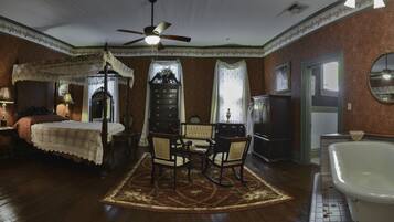 A traditional room with a bed, a sitting area with chairs, a dresser, a mirror, and a bathtub.