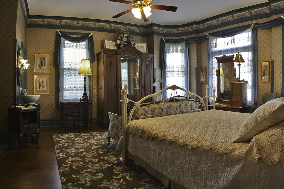 Une chambre à coucher avec un grand lit, une commode en bois, une chaise et un bureau avec une lampe.