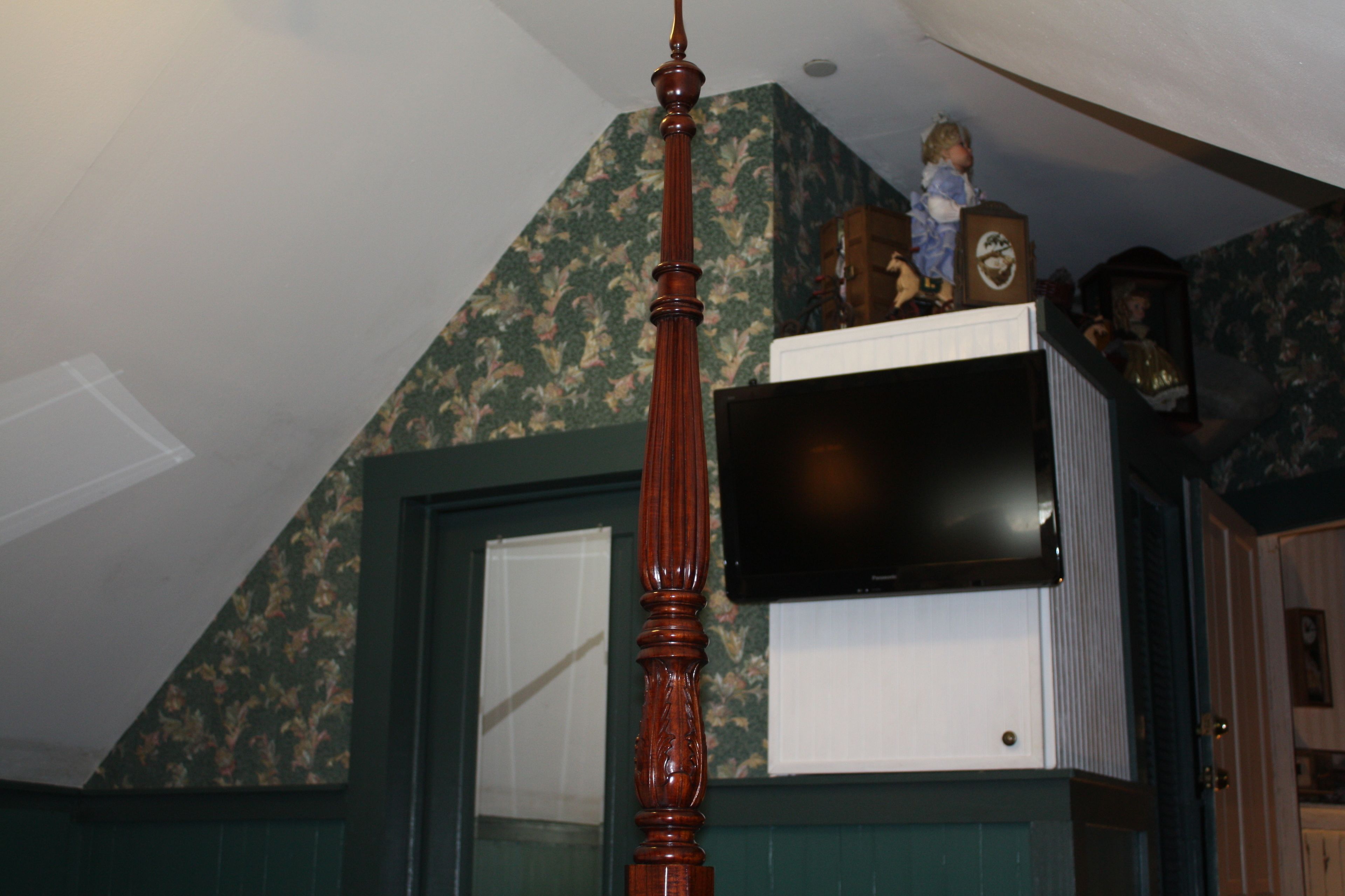 A room with a wooden ceiling fan, a television mounted on a white cabinet, and a doll on top of the cabinet.
