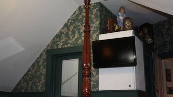 A room with a wooden ceiling fan, a television mounted on a white cabinet, and a doll on top of the cabinet.