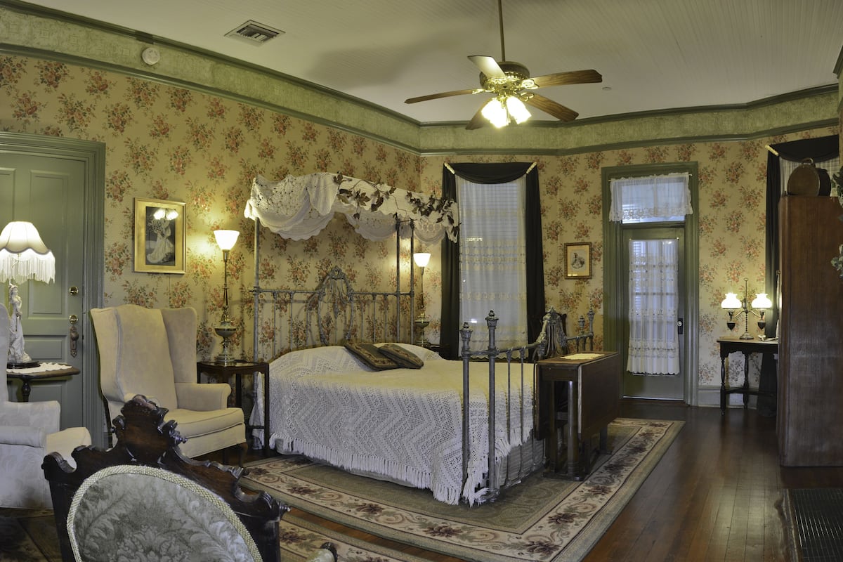 Une chambre à coucher avec un lit à baldaquin, un papier peint à motifs floraux et un ventilateur de plafond.