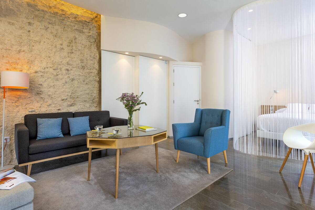 A modern living room with a sofa, a blue armchair, a glass coffee table, and a decorative vase.