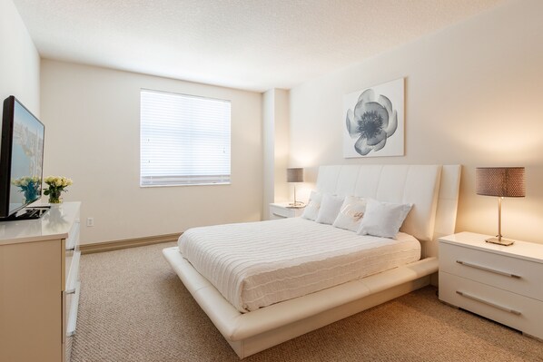 A bedroom with a bed, bedside tables, a lamp, a window, and a wall-mounted artwork.