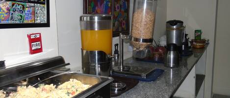 A buffet setup with a variety of food items, a fire safety sign, and a colorful mural on the wall.