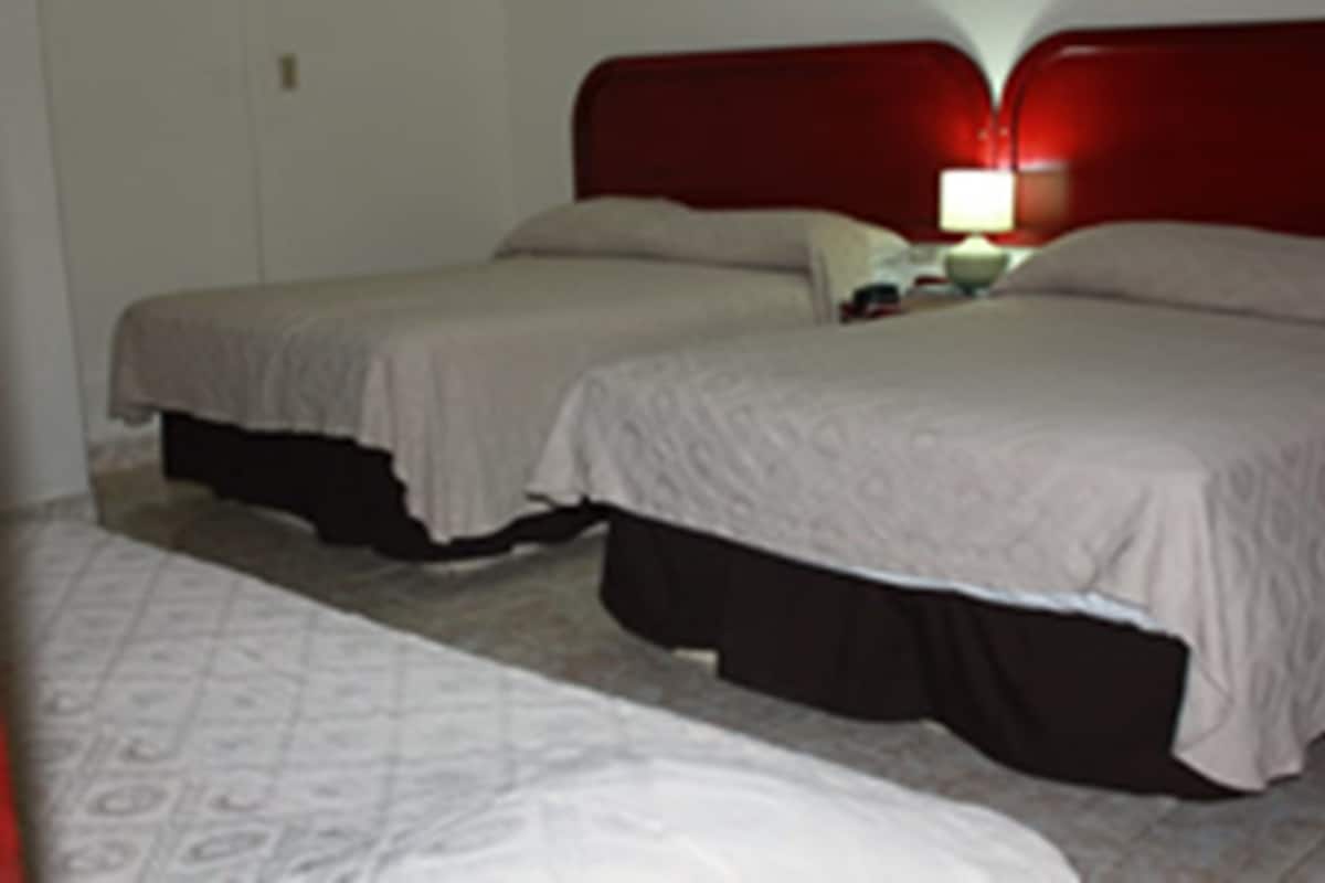 Ein Hotelzimmer mit zwei Einzelbetten, einem roten Kopfteil, einem Nachttisch mit Lampe und Teppichboden.