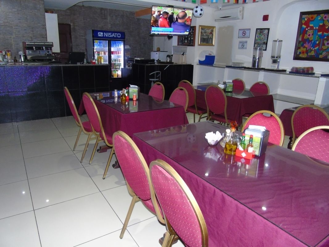 A restaurant with multiple tables and chairs, a counter with a beverage dispenser, and a television screen displaying a program.