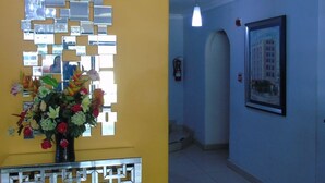 A hallway with a yellow wall, a mirror wall art piece, a framed picture, and a vase with flowers. - Hotel Marparaiso (Panama City)