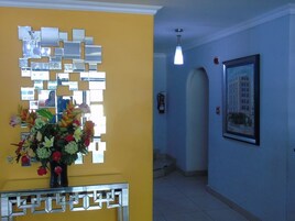 Un pasillo con pared amarilla, una obra de arte de espejo, un cuadro enmarcado y un jarrón con flores.