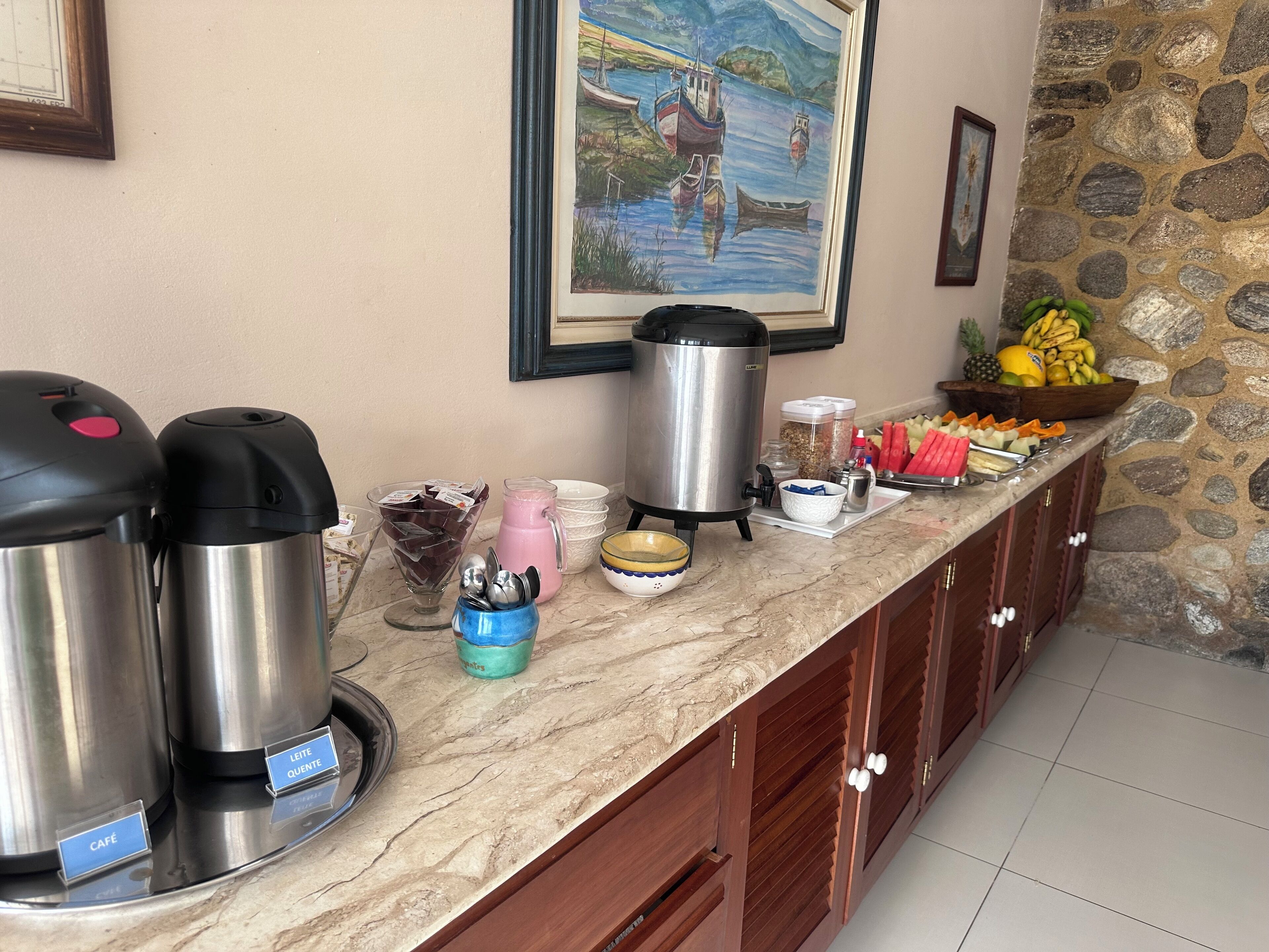 Um balcão de café da manhã com máquinas de café, um jarro e uma cesta de frutas.