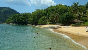 Una playa con agua cristalina, gente nadando y una orilla arenosa con palmeras.