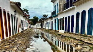 Una calle adoquinada flanqueada por edificios, un charco que refleja la arquitectura, y un cielo despejado.