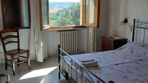 A bedroom with a bed, a chair, a window with a view, a radiator, and a wooden ceiling. - Il Terrazzo delle Rondini (Lapedona)