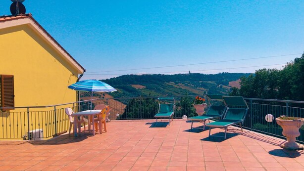 A terrace with a yellow building, outdoor furniture, and a view of green hills. - Il Terrazzo delle Rondini (Lapedona)