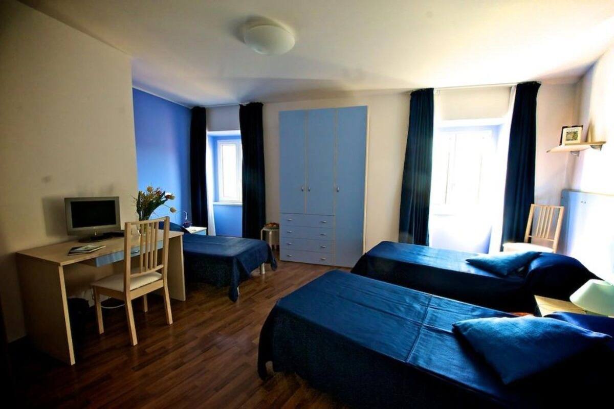 A hotel room with two beds, a desk, a chair, a television, and a wardrobe.