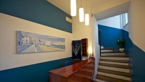 Un espace d’accueil avec un bureau en bois, un tableau représentant un paysage côtier et un escalier aux murs bleus.