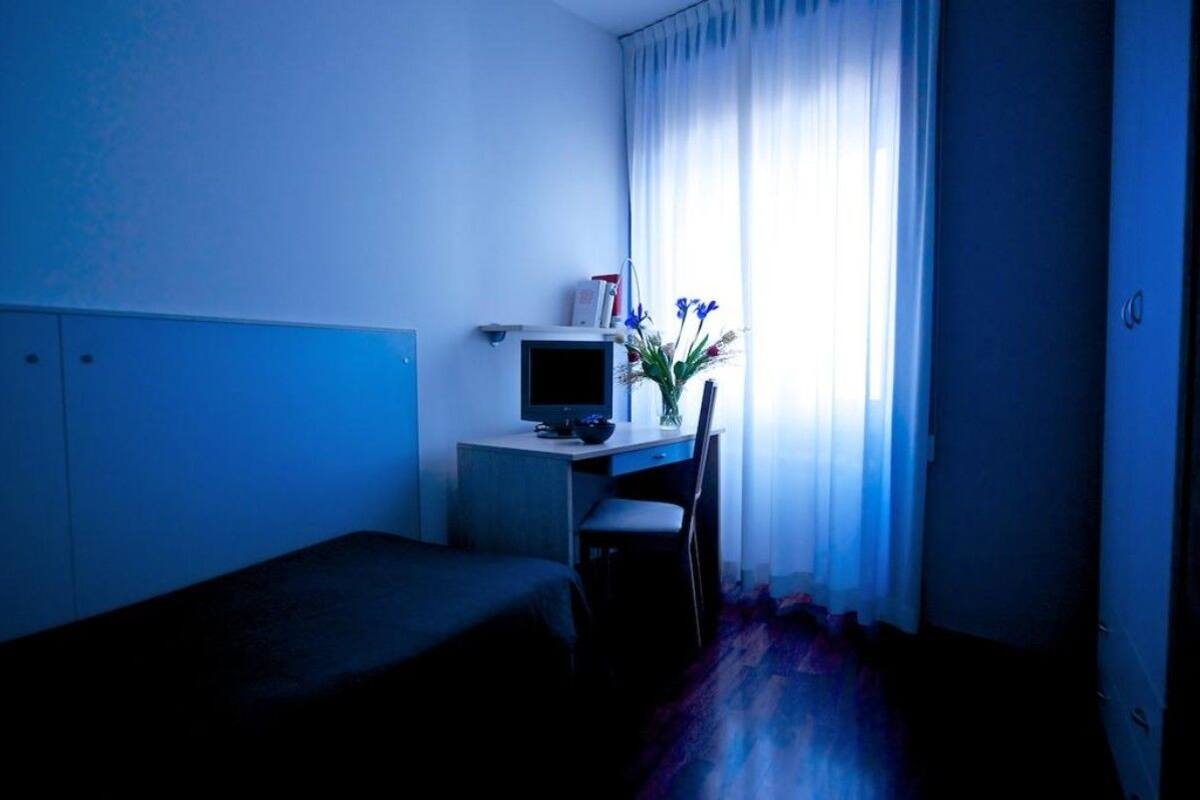A room with a bed, a desk with a computer, and a window with curtains.
