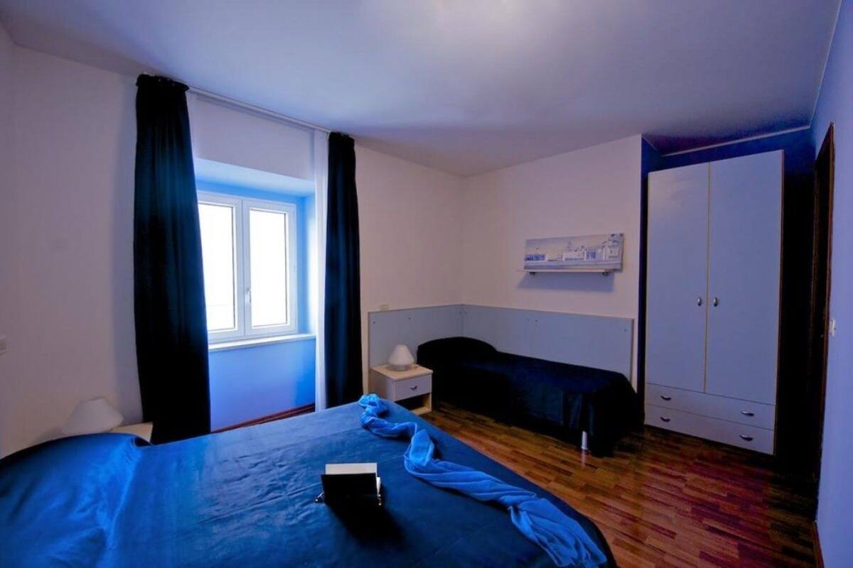 A bedroom with a bed, a nightstand, a wardrobe, and a window with curtains.