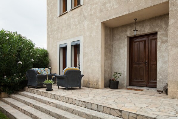 A stone staircase leading to a building entrance with a wooden door, a potted plant, and two wicker chairs with cushions. - Chambres d'hôtes Les villas du triangle (Nîmes)