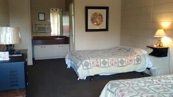 A hotel room with two beds, a desk with a lamp, a microwave, and a framed picture on the wall.