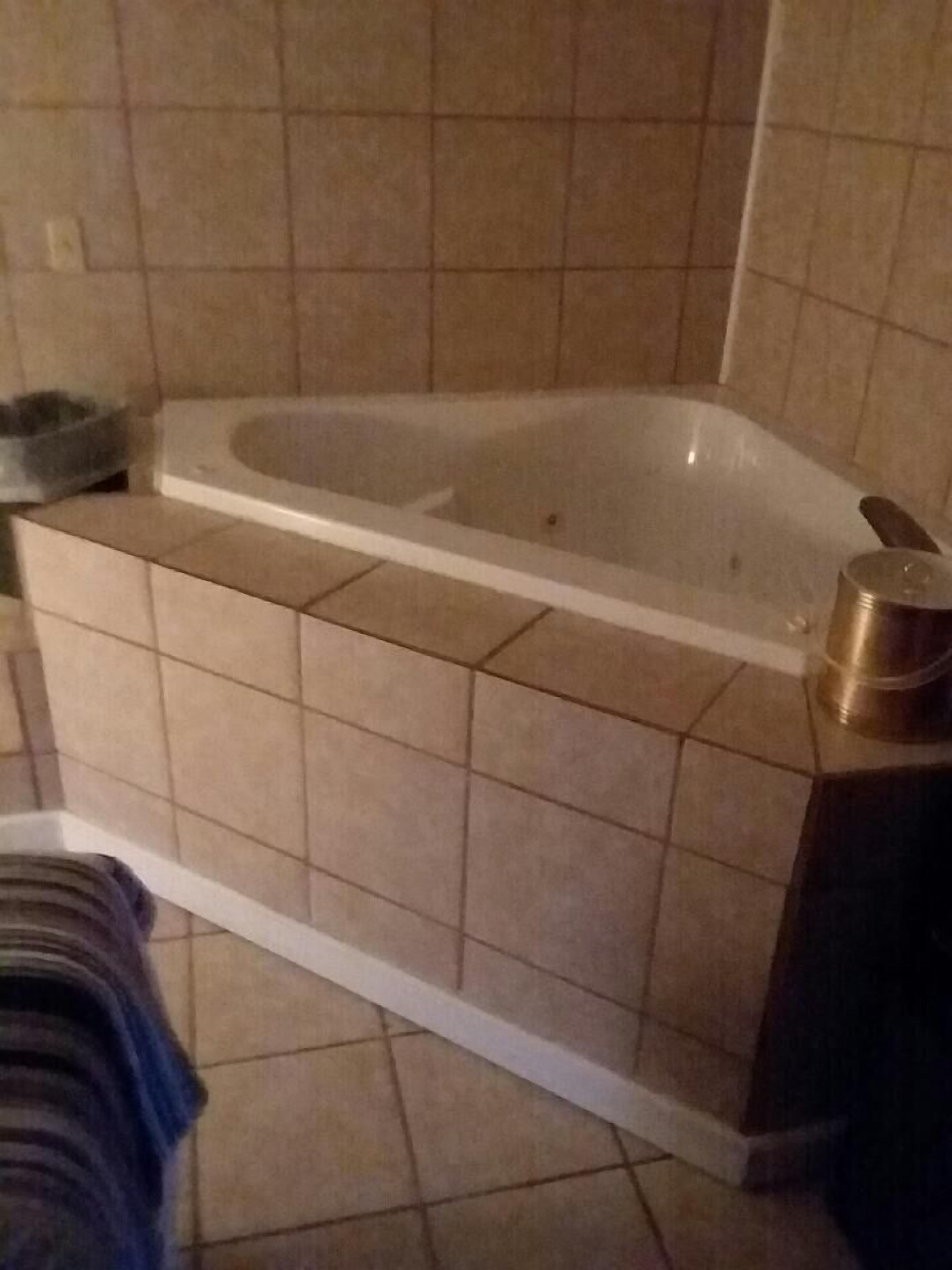 A bathroom with a bathtub, tiled walls, and a metal container on the floor.
