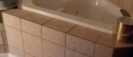 A bathroom with a bathtub, tiled walls, and a metal container on the floor.