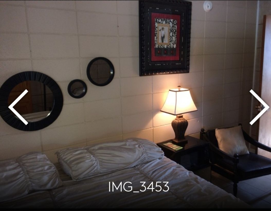 Ein Hotelzimmer mit einem Bett, einem Sessel, einem Nachttisch mit Lampe sowie Wanddekorationen, darunter gerahmte Bilder und Spiegel.