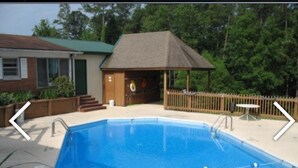 A swimming pool with a wooden deck, a gazebo, and a small building with a green door. - The Resort (Falls of Rough)