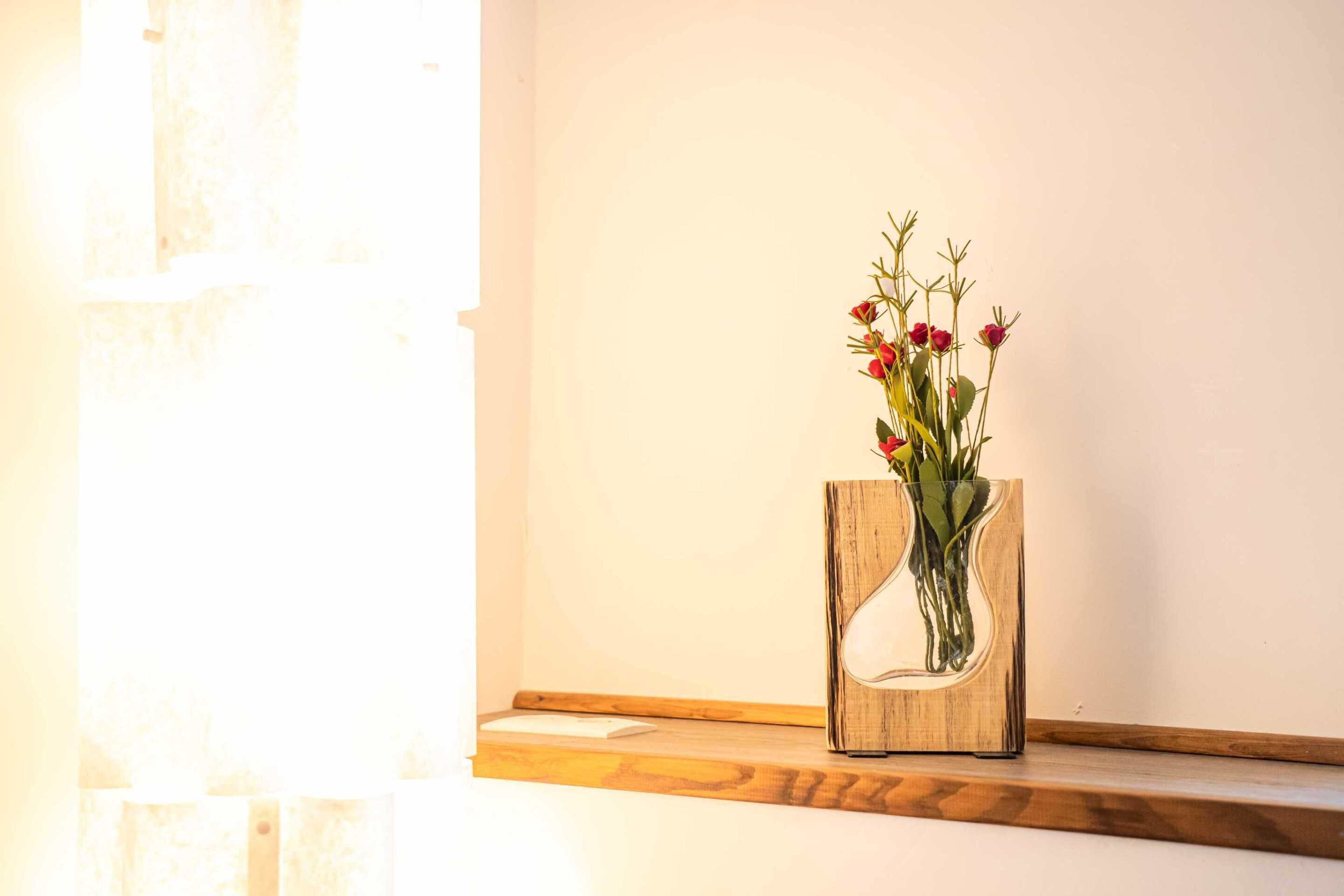 Eine hölzerne Vase mit ungewöhnlicher Form, gefüllt mit roten Blumen, auf einem Holzregal.
