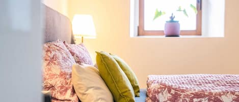 Una cama con ropa de cama floral, una lámpara y una ventana con una planta.