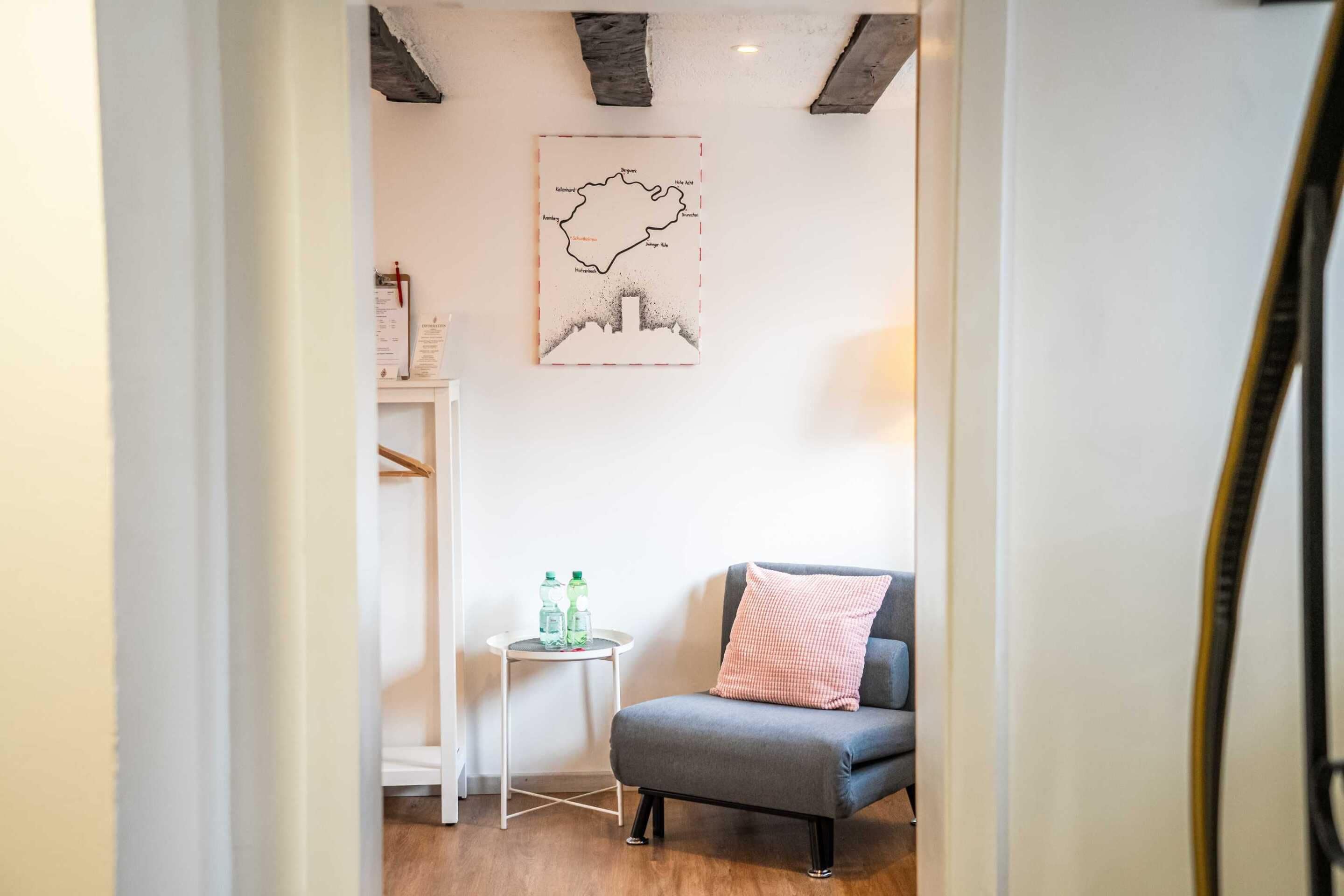 A room with a grey armchair, a small white table with water bottles, and a framed map on the wall.