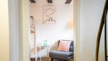 A room with a grey armchair, a small white table with water bottles, and a framed map on the wall.